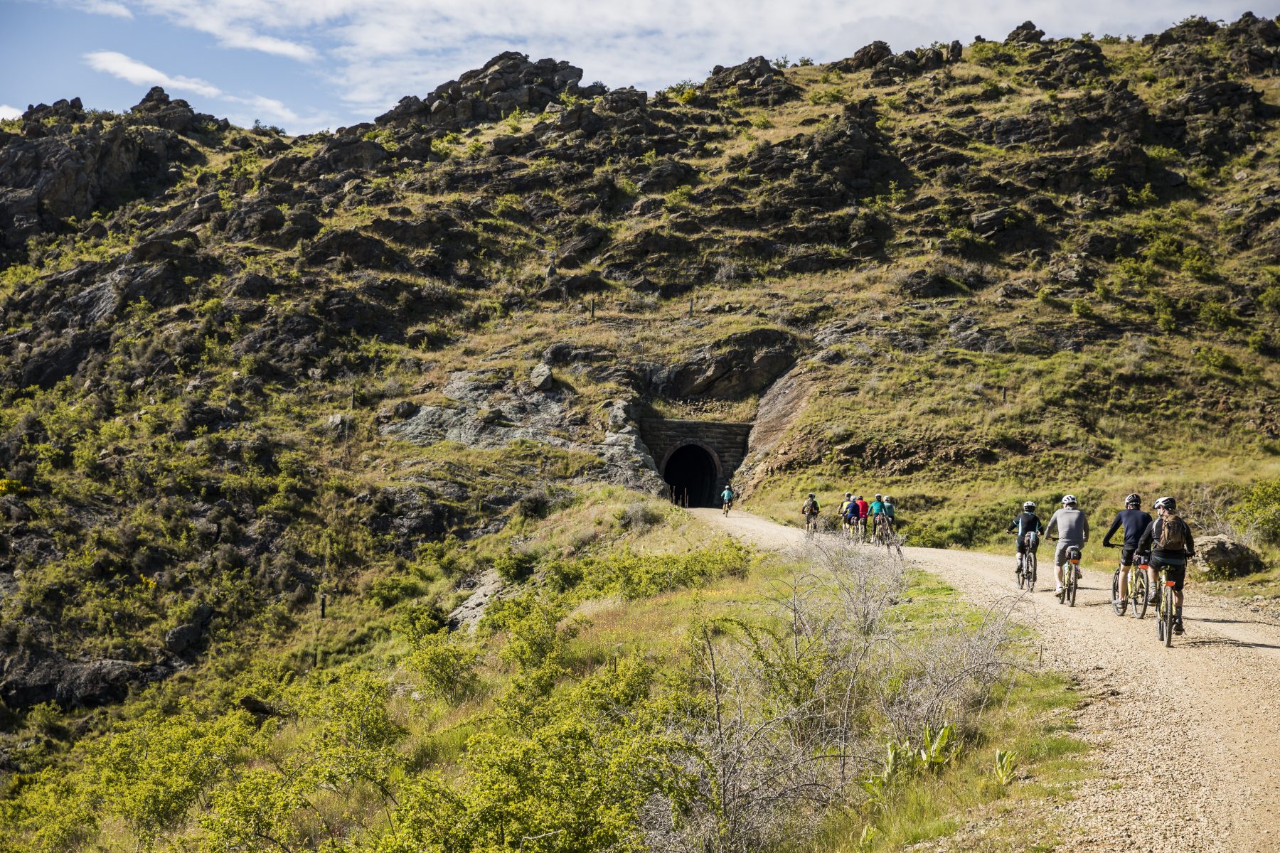 A group riding towards a stone tunnel on the Otago Central Rail Trail