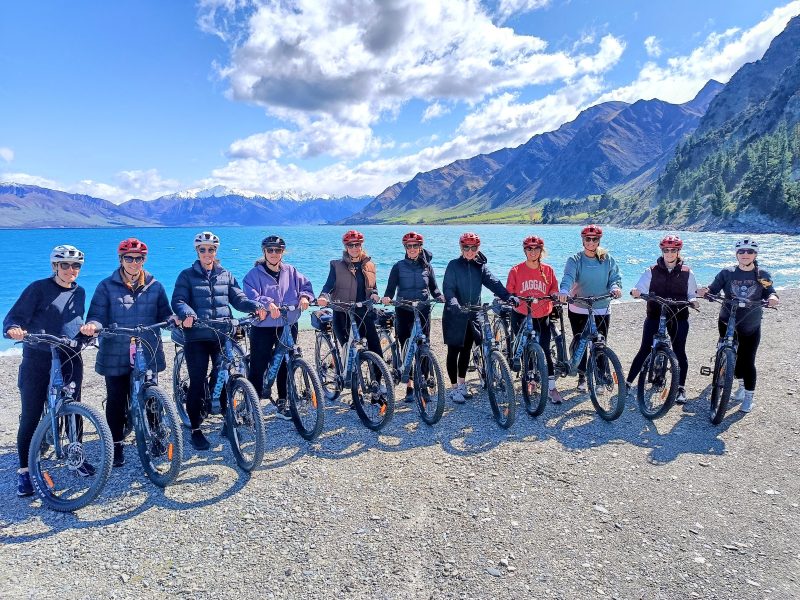 A group lined up with their e-bikes beside Lake Dunstan
