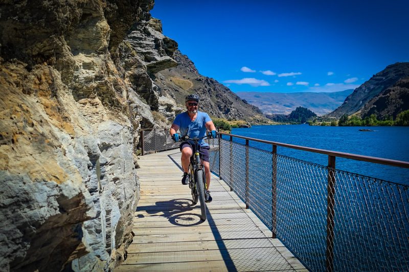 A rider on a Sinch e-bike crossing the clip-on boardwalk above Lake Dunstan