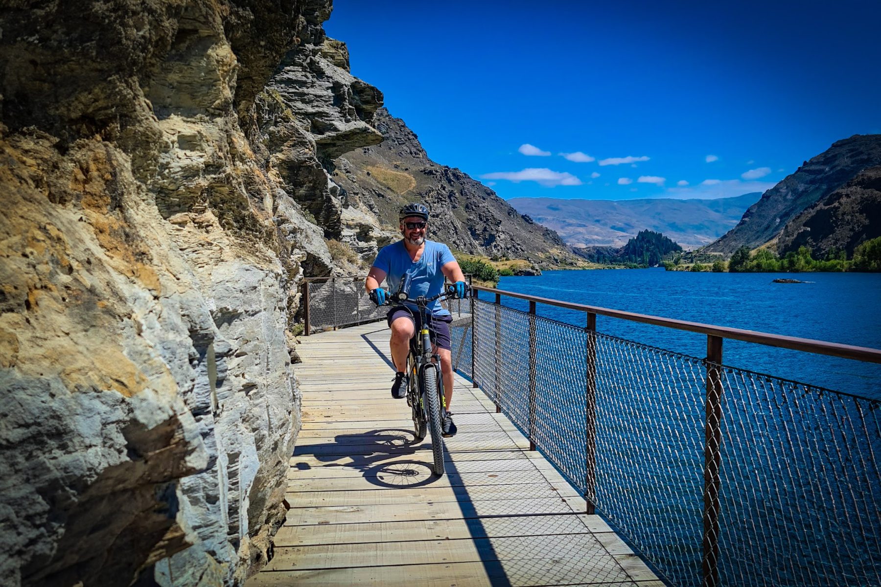 A rider on a Sinch e-bike crossing the clip-on boardwalk above Lake Dunstan