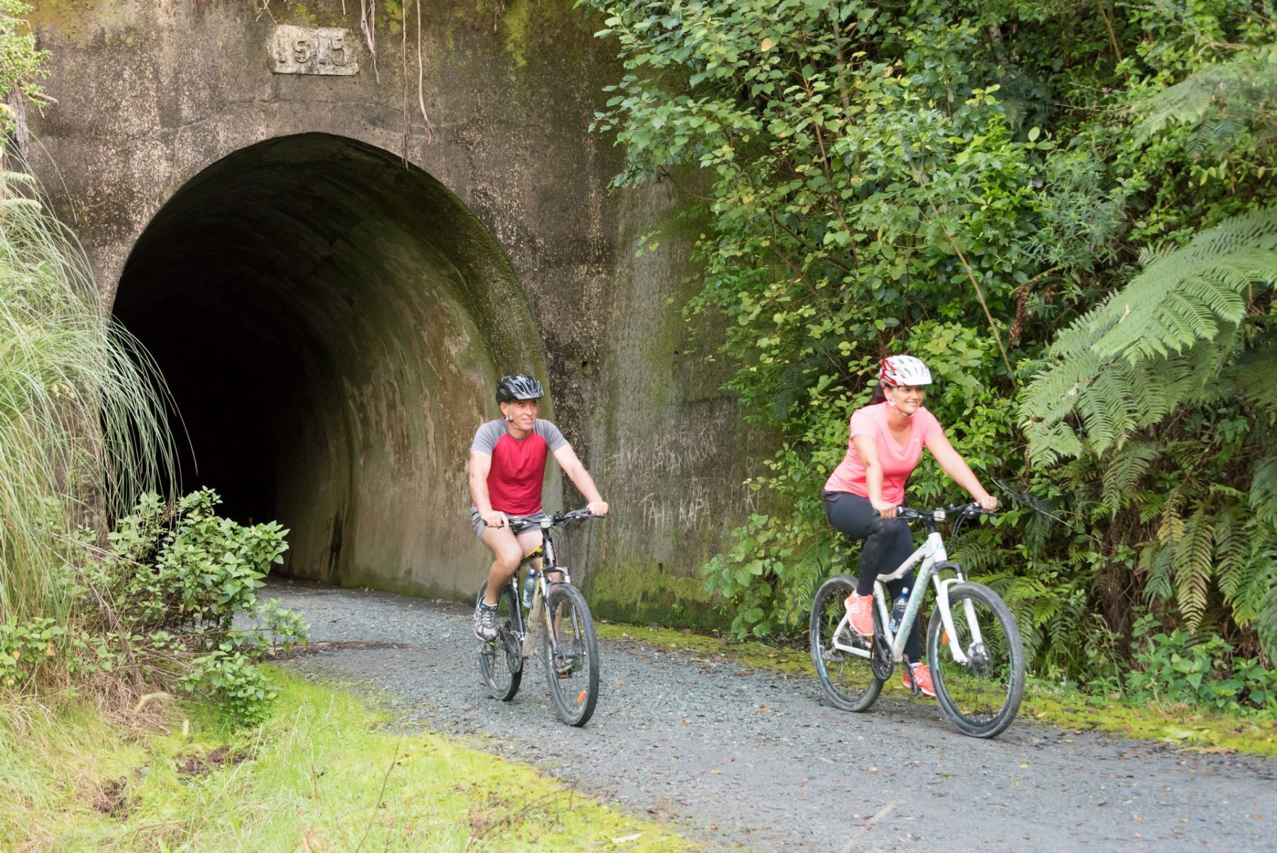 Two riders coming out of the old railway tunnel on the Twin Coast Cycle Trail