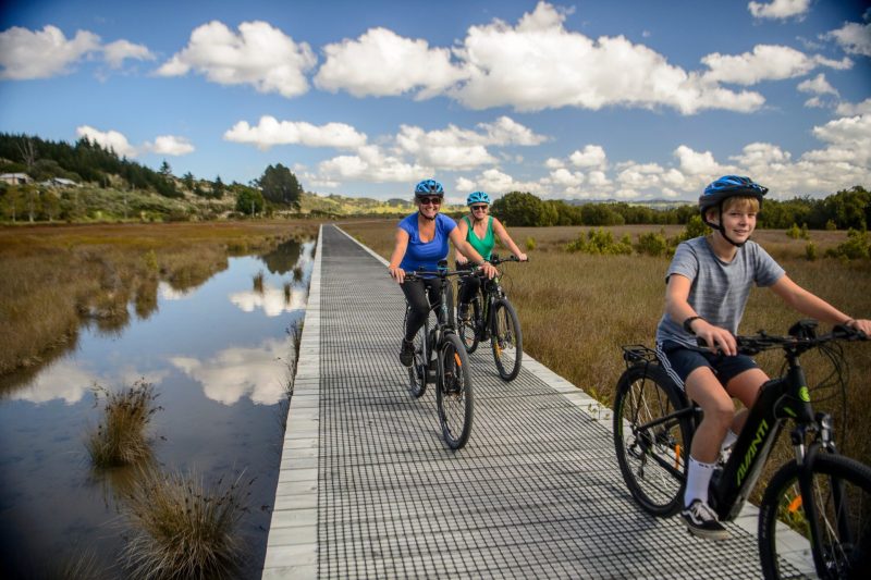 Riders on the boardwalk across the wetland on the Twin Coast Cycle Trail